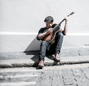 A guitarist plays while sitting down on a pavement